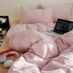 a laptop computer sitting on top of a bed covered in pink and white striped sheets