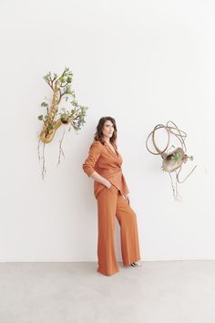 a woman in an orange jumpsuit standing next to a wall with plants on it