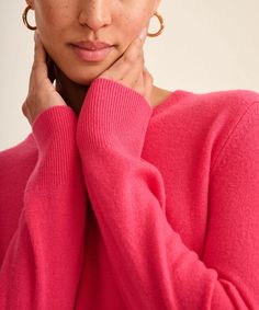 a woman in a pink sweater is posing with her hand on her chin and looking at the camera