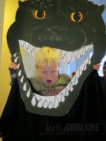 a young boy in a t - shirt is holding up a cardboard alligator mask to his face