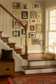 a staircase with pictures on the wall and a basket sitting on top of it in front of a window