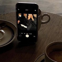 a cell phone sitting on top of a wooden table next to two cups of coffee