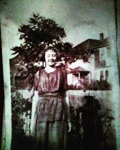 an old photo of a woman standing in front of a tree