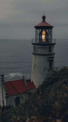 a light house sitting on top of a lush green hillside next to the ocean under a cloudy sky