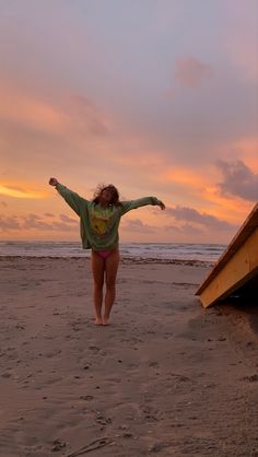 a woman standing on top of a sandy beach next to a surfboard under a cloudy sky