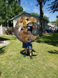 a man is standing in the grass holding a large metal object that looks like a woman's face