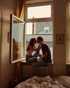 two people sitting on a window sill next to each other in front of a bed