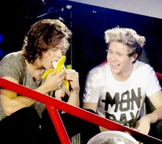 two young men sitting next to each other with bananas in their hands and one holding a banana