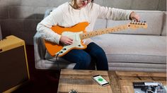 a woman sitting on a couch with an orange guitar in front of her, playing the guitar