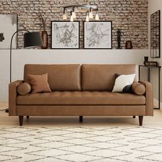 a brown couch sitting in front of a brick wall with two framed pictures on it