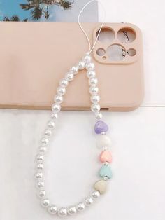 a white beaded necklace sitting on top of a table next to a cell phone