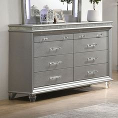 a silver dresser sitting in front of a mirror on top of a wooden floor next to a vase with flowers