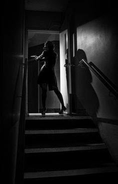 a woman walking up some stairs in the dark with her hand on an open door