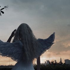a woman with long white hair standing in front of the sun wearing an angel costume