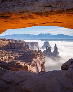 an arch in the side of a mountain with low clouds below it and mountains beyond