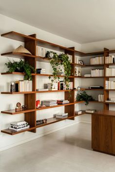 a living room filled with lots of books and plants on wooden shelves next to a desk