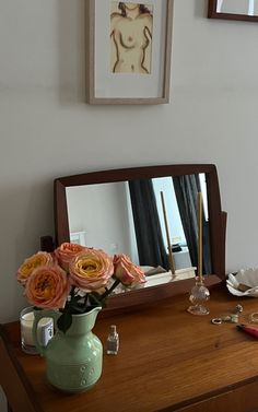 a vase with flowers sitting on top of a wooden table next to a mirror and other items