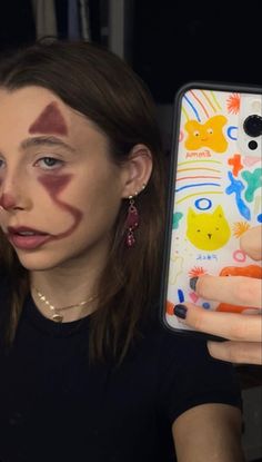 a woman holding up a phone with her face painted like a cat and dog on it