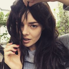 a woman with long dark hair is brushing her bangs