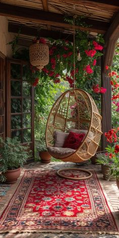 a hanging chair on a porch with flowers and potted plants in the back ground