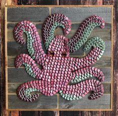 a pink and green octopus made out of bottle caps on a wooden planked wall