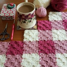 a crocheted blanket, yarn and scissors are sitting on a table next to a mug
