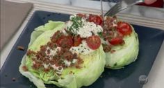 lettuce topped with tomatoes and other toppings being cut into wedges on a blue plate