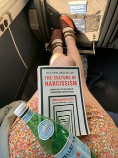 a person laying on an airplane seat with a book and water bottle in their lap