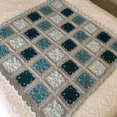 a crocheted blanket on top of a bed next to a white and blue pillow