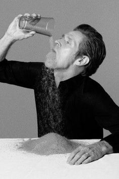 a man drinking from a bottle while sitting at a table with his head in the air