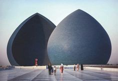 several people are walking around in front of two large blue domes that look like giant balls