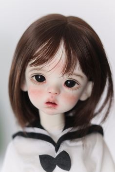 a doll with brown hair wearing a white shirt and black bow tie on it's neck