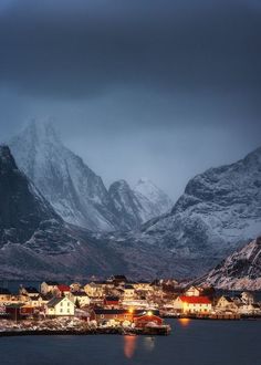 the mountains are covered in snow and lit up by lights on houses, buildings, and boats