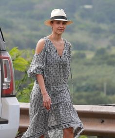 a woman in a dress and hat walking towards a car