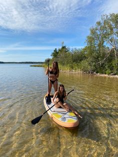 two women in bikinis paddling on a paddle board with one standing up and the other sitting down