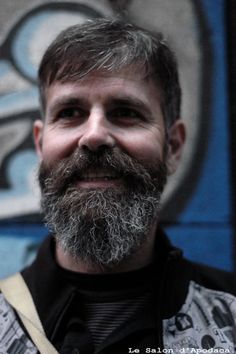 a close up of a person with a beard and wearing a vest in front of a graffiti wall