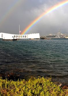 a rainbow in the sky over a large body of water with a building on it