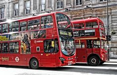 two red double decker buses parked next to each other in front of a tall building