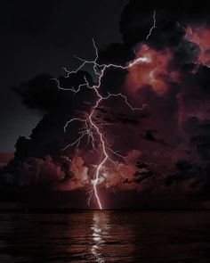 a lightning bolt is seen in the sky over water at night with dark clouds and bright lights
