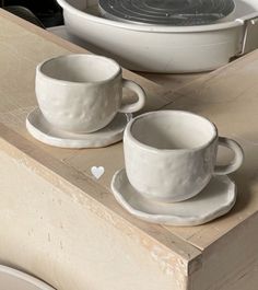 two white cups and saucers sitting on top of a wooden table next to a stove