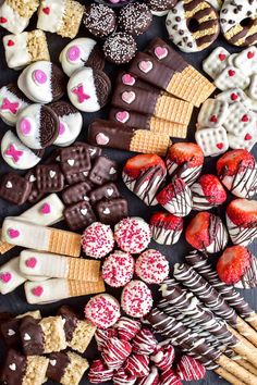 an assortment of heart shaped cookies and desserts arranged on a table with strawberries