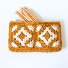 an orange crocheted pot holder with wooden knitting needles in it next to a white background