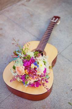 a guitar sitting on the ground with flowers in it
