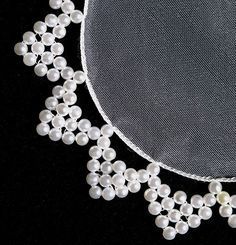 a white necklace with pearls is displayed on a black tablecloth and net to the side