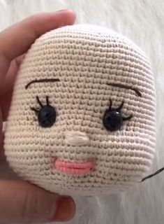 a hand is holding a small white doll with black eyes and eyelashes on it's face