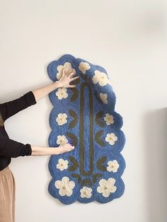 a woman standing next to a blue rug with white flowers on it and reaching up