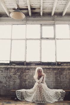 a woman in a long white dress sitting on a wooden floor next to windows and a light fixture