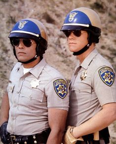 two police officers standing next to each other in front of a rocky mountain side area