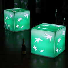 two illuminated cubes sitting on top of a wooden floor next to a wine bottle
