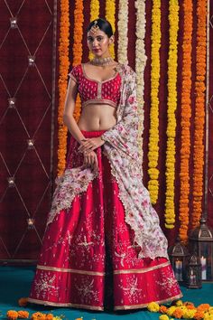 a woman in a red and white lehenga with flowers on the wall behind her